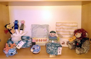 Regal mit handgemachtem Kinderspielzeug, Taschen und Strickwaren.