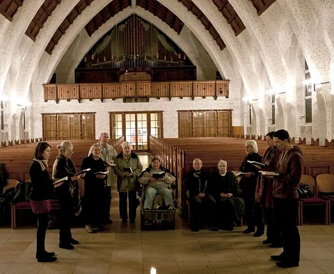 Menschen singen in einer Kirche, um eine brennende Kerze versammelt.