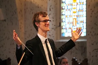 Lächelnder Dirigent mit Taktstock, leitet Chor oder Orchester.