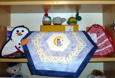 Regal mit Handarbeiten: Schneemann, gesteppte Matte mit Mond, Nadelkissen.