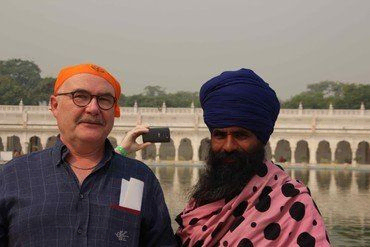 Zwei Männer, einer mit orangem Turban, der andere mit blauem Turban, am Wasser.