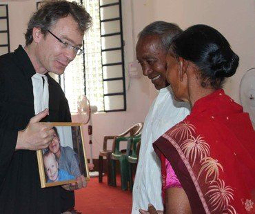 Pastor zeigt einem älteren Ehepaar ein gerahmtes Foto von Kindern.