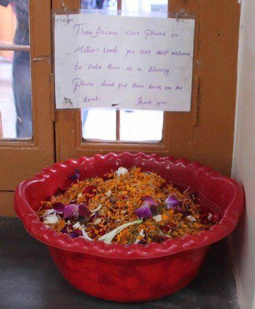 Rote Schale mit Blumenopfern und handschriftlichem Schild darüber.