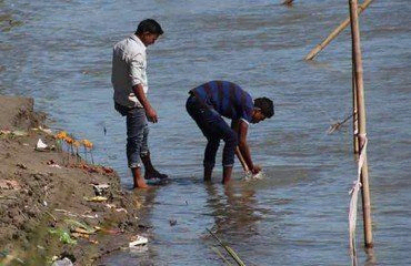 Zwei Männer am Fluss, einer bückt sich, um das Wasser zu berühren.