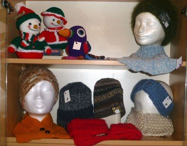 Auslage von gestrickten Wintermützen, Schals und Schneemann-Dekorationen.
