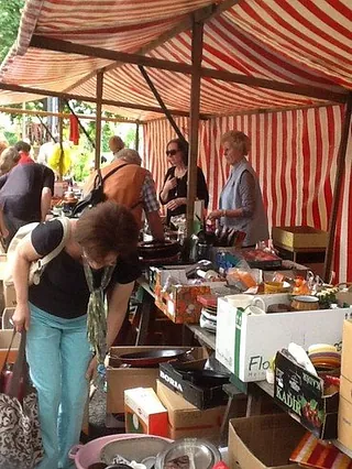 Menschen stöbern unter einem gestreiften Marktstand-Dach.