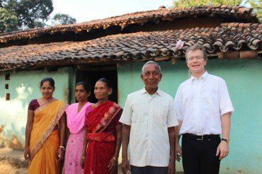 Pastor steht lächelnd mit vier indischen Dorfbewohnern vor einem Haus.