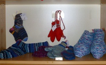 Handgestrickte Socken, Fäustlinge und Hausschuhe in Regalen ausgestellt.