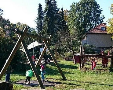 Kinder spielen auf Schaukeln und Spielgeräten in einem sonnigen Garten.