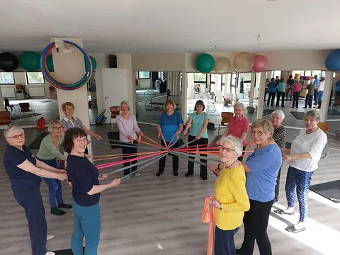 Gruppe älterer Frauen trainiert mit Widerstandsbändern in einem Fitnessraum.