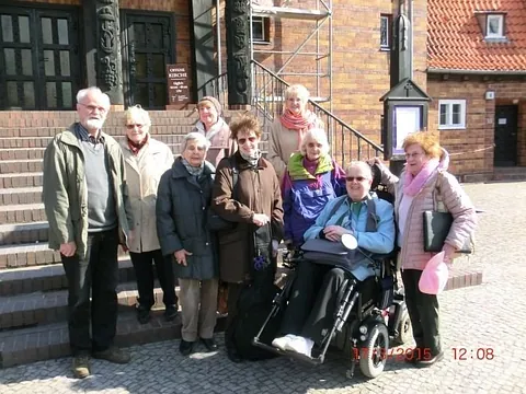 Gruppe verschiedener älterer Erwachsener, einer im Rollstuhl, vor einer Kirche.