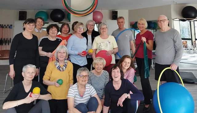 Gruppe verschiedener Personen, meist Senioren, mit Sportgeräten in einem Fitnessraum.