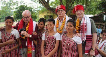 Gruppe von Personen, einige in traditioneller Kleidung und Girlanden, posieren im Freien.