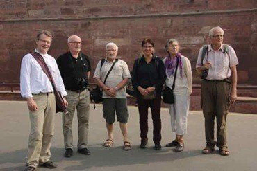 Gruppe von sechs Touristen steht vor einer roten Ziegelmauer.